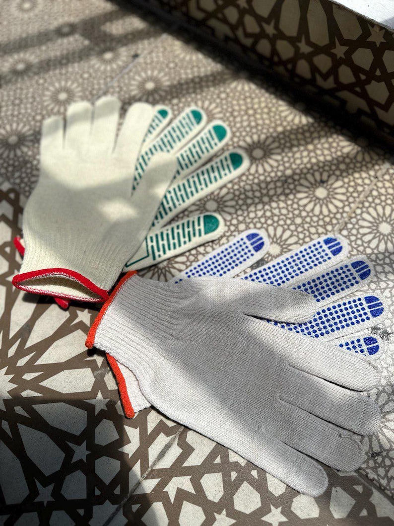 May include: Two pairs of work gloves. One pair is light gray with red trim and blue dotted grips. The other pair is off-white with green grips and red trim. The gloves are made of a knitted material.