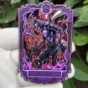 May include: A rectangular purple enamel pin featuring a stylized illustration of a character with a helmet and armor, surrounded by fiery orange and purple effects. The pin has the word "BERU" at the bottom.