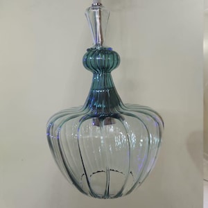 May include: A clear glass pendant light with a teal-colored top and a bulbous, ribbed body. The light fixture hangs from a white cord and features a decorative, elongated top.