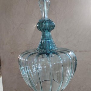 May include: A clear, teal-colored glass pendant light fixture. The light has a bulbous, ribbed shade and a slender, decorative top. The fixture is suspended by a white cord, showcasing a vintage or art deco design.