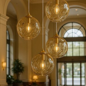 May include: Four pendant lights with amber-colored, globe-shaped glass shades. Each light has a gold-colored metal fixture and a visible lightbulb. The glass shades have a textured, swirling design. The lights hang in a well-lit interior space.