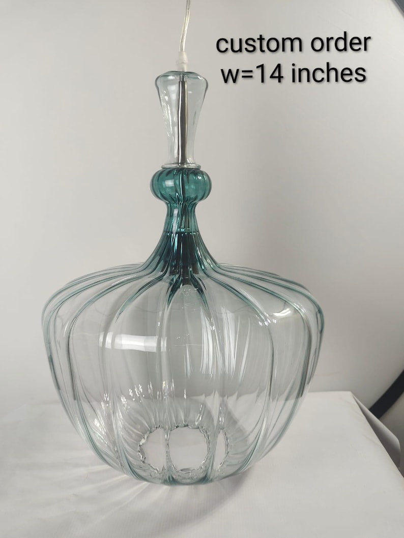 May include: Clear glass pendant light with teal accents and a ribbed design. The light fixture has a width of 14 inches and a decorative top. The text "custom order" is visible.
