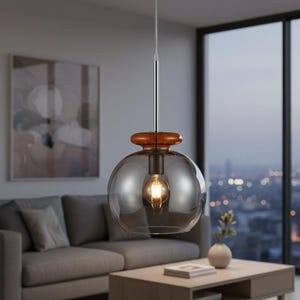 May include: A modern pendant light with a smoky gray glass globe shade and a warm, glowing bulb. The light fixture has a brown wooden accent and a silver rod. The light hangs in a living room with a gray sofa and a wooden coffee table.