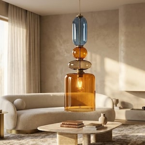 May include: A pendant light fixture featuring a vertical stack of four glass elements in blue and amber tones, suspended by a brass-colored rod. The bottom component is a large amber cylinder housing a single light bulb, topped by three smaller, rounded glass shapes in amber and blue hues.