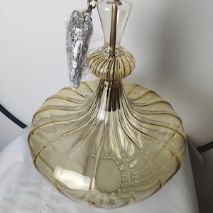 May include: A vintage-style pendant light fixture with a clear glass and gold-toned metal design. The light has a rounded, ribbed shade and a decorative top with a chain for hanging. The glass has a warm, amber hue.