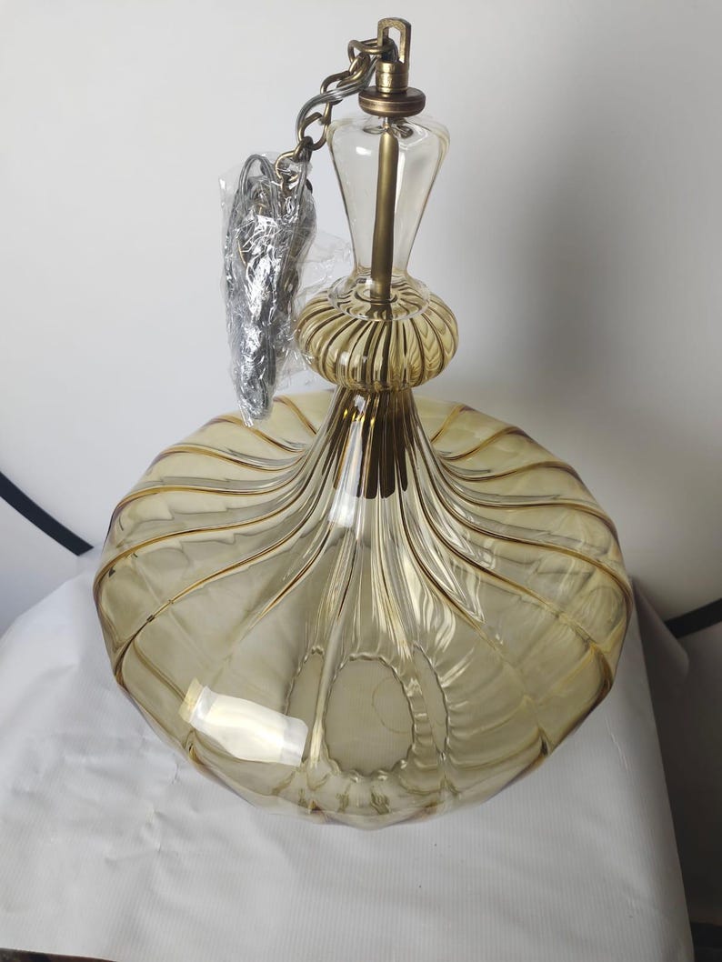 May include: A vintage-style pendant light fixture with a clear glass and gold-toned metal design. The light has a rounded, ribbed shade and a decorative top with a chain for hanging. The glass has a warm, amber hue.