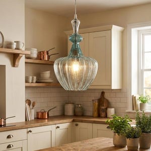 May include: A clear glass pendant light with a ribbed design and a light blue top. The light hangs from a thin wire and illuminates a kitchen with wooden countertops and white cabinets. The light fixture is a decorative element.