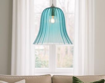 May include: A turquoise glass pendant light with a bell-shaped shade hangs from the ceiling. The shade has vertical ridges and a flared bottom. A lit bulb is visible inside. The light hangs above a beige sofa with pillows.