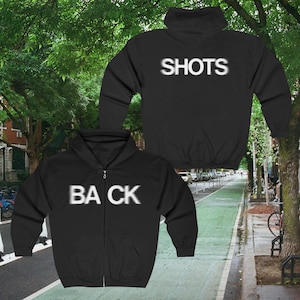 May include: Black zip-up hoodie with the word "SHOTS" printed on the back and the word "BACK" printed on the front.