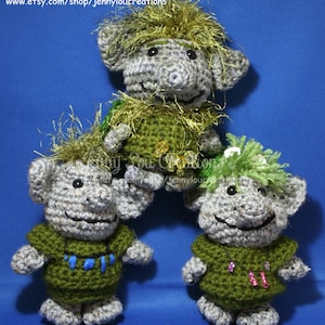May include: Three crocheted troll dolls with green and gray yarn. The trolls have green shirts with beads and gold yarn hair. The trolls are on a blue background.