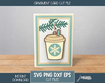 May include: A greeting card with a coffee cup ornament cut file design. The ornament is a beige coffee cup with a snowflake and a brown lid. The card has a teal and beige border and a sprig of evergreen. The text "Ornament Card Cut File" is at the top.