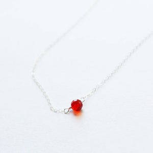 Puede incluir: Un delicado collar de cadena de plata con un solo colgante de piedra roja.