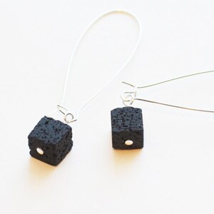 May include: A pair of silver dangle earrings with black lava rock cube charms. Each cube has a small silver bead in the center.