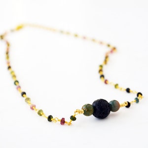 May include: A gold chain necklace with small multi-colored beads and a larger black lava rock bead.