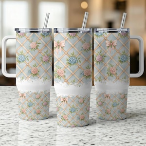 Könnte beinhalten: Drei Edelstahl-Reisebecher mit Griffen und Strohhalmen. Die Becher haben einen hellblauen Hintergrund mit einem Gittermuster, rosa Schleifen und Blumendesigns in Rosa, Blau und Grün. Ein weißer, spitzenartiger Rand akzentuiert den Boden.