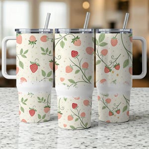 Könnte beinhalten: Drei weiße isolierte Becher mit Griffen und Deckeln. Jeder Becher hat ein sich wiederholendes Muster aus roten Erdbeeren, grünen Blättern und Ranken auf cremefarbenem Hintergrund. Silberne Strohhalme sind in die Deckel gesteckt.