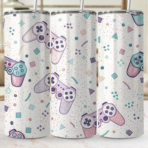 May include: A cylindrical stainless steel tumbler with a white background featuring a repeating pattern of light purple and teal video game controllers, small geometric shapes, and scattered dots, topped with a clear lid and a metal straw.