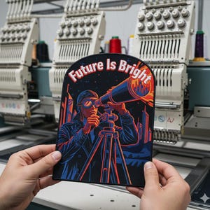 May include: A black patch with the words "Future Is Bright" in red and white. The patch features a person looking through a telescope with a city skyline in the background. The patch is held in front of an embroidery machine.