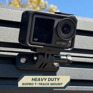 Puede incluir: Cámara de acción negra con el texto "ACTION 4" montada en un soporte GoPro T-track resistente. El soporte está fijado a una superficie texturizada. El texto "HEAVY DUTY" y "GOPRO T-TRACK MOUNT" se muestra en una pancarta.