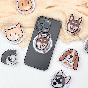 May include: A set of phone ring holders featuring various animal illustrations. The holders are clear with a white ring and a colorful animal face in the center. The animals include a cat, a dog, a husky, and a poodle. Each holder has a name printed below the animal.