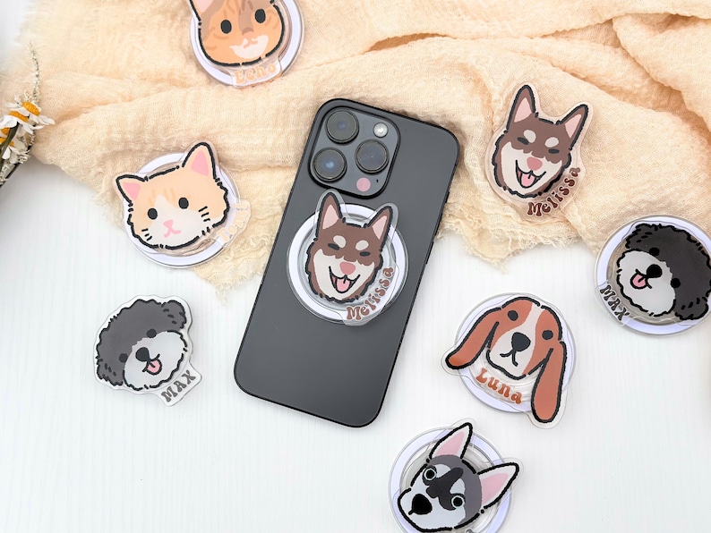 May include: A set of phone ring holders featuring various animal illustrations. The holders are clear with a white ring and a colorful animal face in the center. The animals include a cat, a dog, a husky, and a poodle. Each holder has a name printed below the animal.