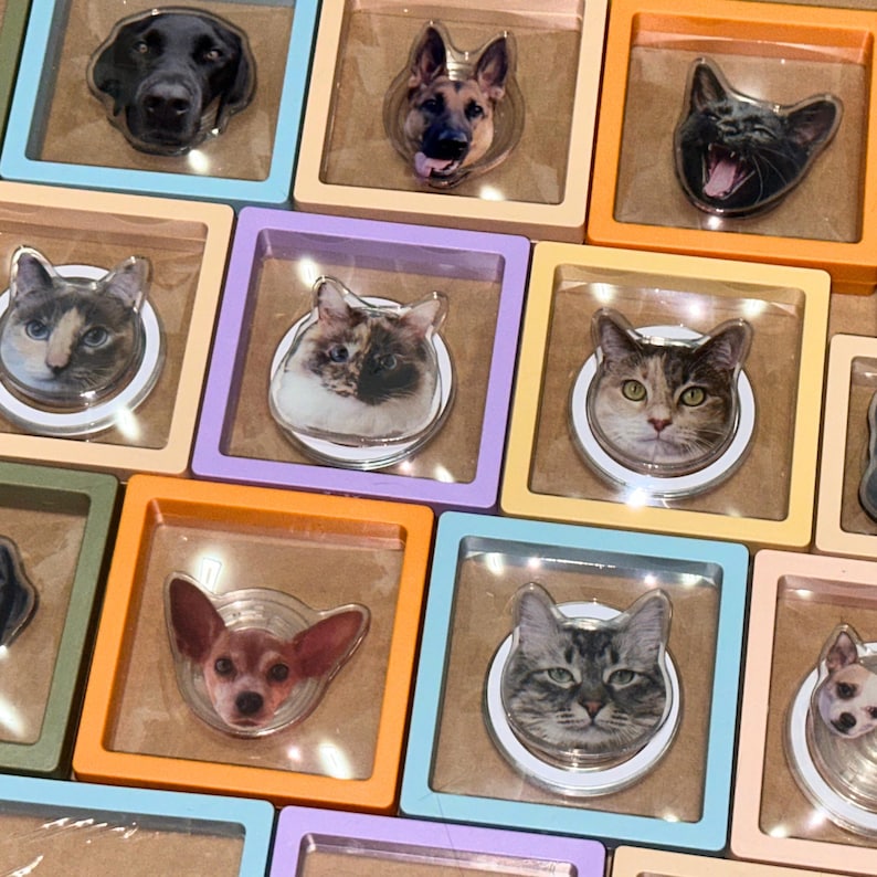 May include: A collection of colorful phone grips with different animal images. The grips are in various colors, including purple, orange, blue, and green. The animal images include a cat, a dog, and a chihuahua.
