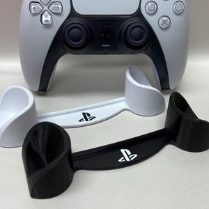 May include: Two different PlayStation controller stands. One is white and the other is black. Both stands feature the PlayStation logo.