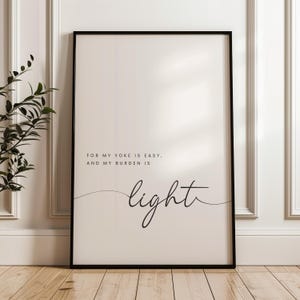 May include: Framed art print with a black frame. The print has a cream-colored background with the words "For my yoke is easy, and my burden is light" in black text. The word "light" is in a cursive font.