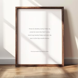 Puede incluir: Un marco rectangular de madera marrón oscuro que contiene una impresión blanca con texto negro estilo máquina de escribir. El texto dice: Prone to wander, Lord, I feel it, prone to leave the God I love; here's my heart; O take and seal it; seal it for thy courts above. Bind my wandering heart to thee.