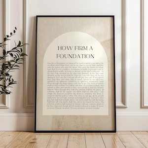 Puede incluir: Impresión artística enmarcada con el texto "HOW FIRM A FOUNDATION" en un marco negro. La impresión presenta un fondo beige con una gran forma de arco en la parte superior. El texto está en una fuente serif clásica.