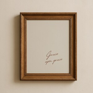 May include: A rectangular wooden picture frame with a medium brown finish and a multi-layered grooved border. Inside the frame, a light beige mat surrounds a central area featuring the dark brown cursive text Grace upon grace printed clearly.