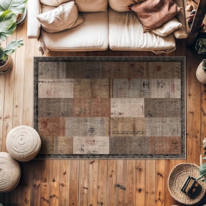 May include: Rectangular rug with a patchwork design in shades of brown, beige, and red. The rug has a dark border and is placed on a wooden floor. The rug is under a cream-coloured sofa with pillows and plants.