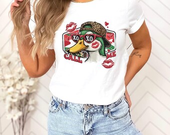 May include: White t-shirt featuring a cartoon duck wearing sunglasses and a leopard print hat. The duck has a yellow beak and is surrounded by red lips and hearts. The text "CALL ME XO XO" is also on the shirt.