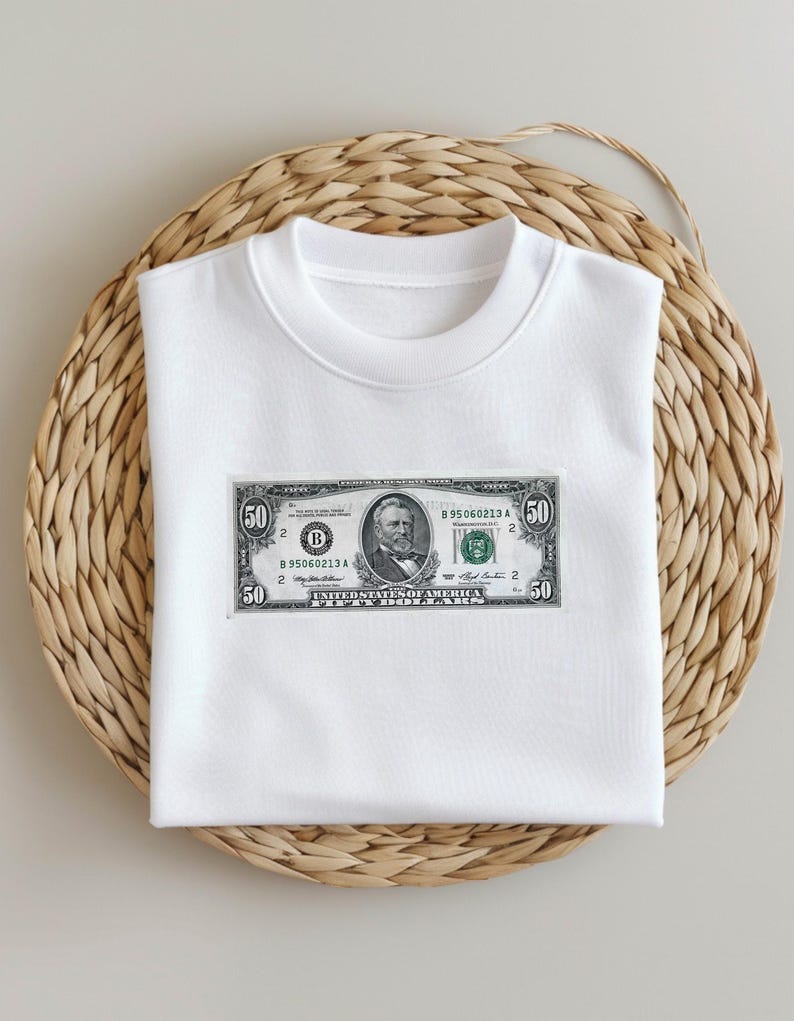 May include: White t-shirt with a printed image of a $50 bill featuring Abraham Lincoln. The bill has the serial number B 895060213 A.