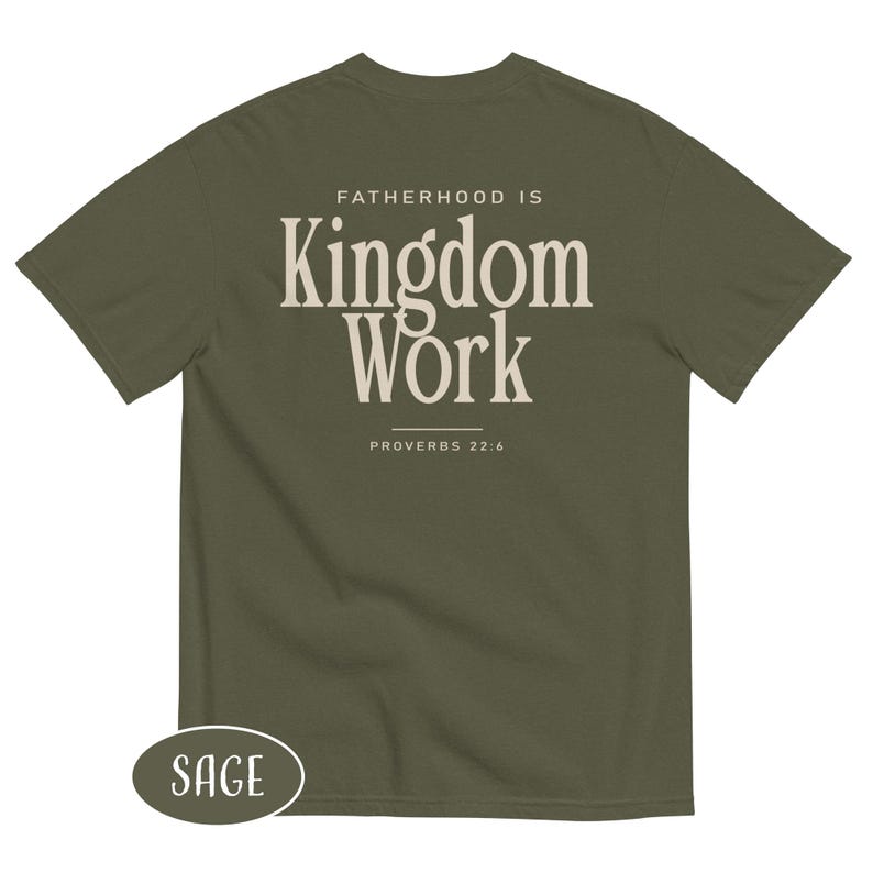 May include: Sage green t-shirt with the text "FATHERHOOD IS Kingdom Work" in a cream-colored font. The text "PROVERBS 22:6" is below the main text. A small oval label at the bottom left says "SAGE".