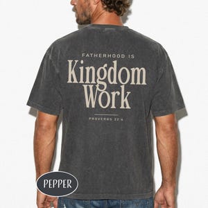 May include: Dark gray t-shirt with the text "FATHERHOOD IS Kingdom Work" and "PROVERBS 22:6" printed on the back. The shirt has a vintage, worn look. The brand name "PEPPER" is printed on the bottom left.