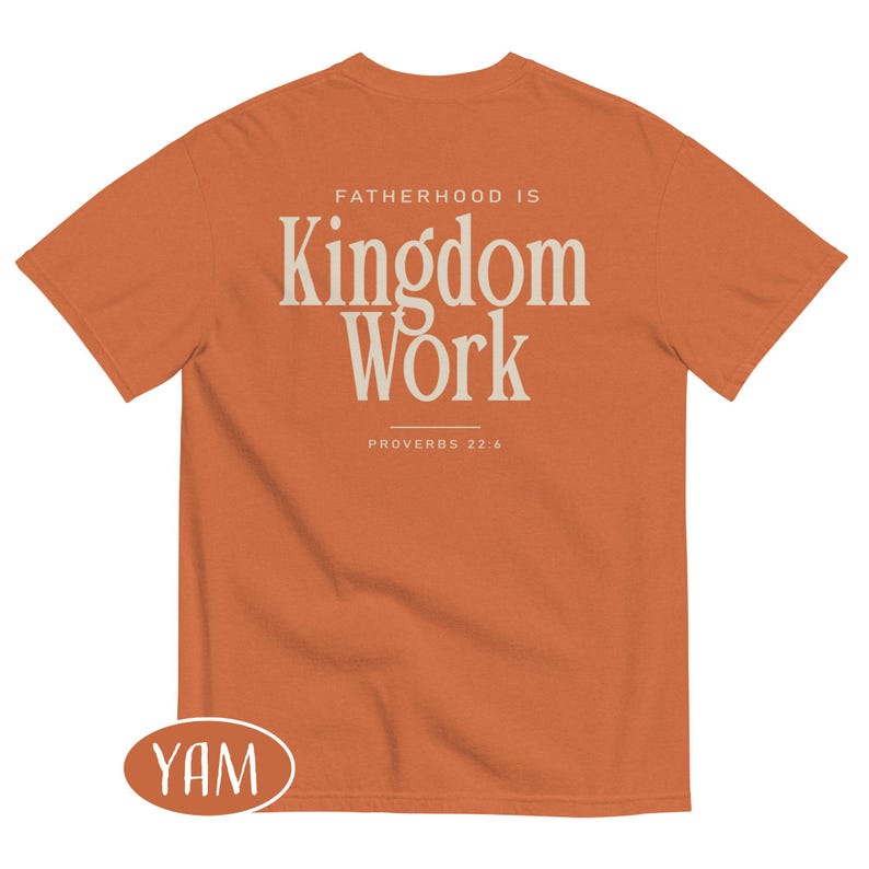 May include: An orange t-shirt with the text "FATHERHOOD IS Kingdom Work" in a cream-colored font. The text "PROVERBS 22:6" is below the main text. The shirt is a short-sleeved crew neck.