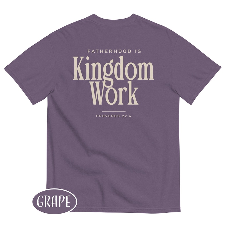 May include: A grape-colored t-shirt with the text "FATHERHOOD IS Kingdom Work" in a cream-colored font. The text "PROVERBS 22:6" is below the main text. The word "GRAPE" is in a white oval at the bottom left.