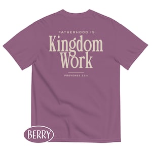 May include: Berry-colored t-shirt with the text "FATHERHOOD IS Kingdom Work" in a cream-colored font. The text "PROVERBS 22:6" is below the main text. The shirt has a crew neck and short sleeves. The word "BERRY" is in a berry-colored oval at the bottom.