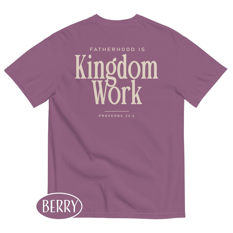 May include: Berry-colored t-shirt with the text "FATHERHOOD IS Kingdom Work" in a cream-colored font. The text "PROVERBS 22:6" is below the main text. The shirt has a crew neck and short sleeves. The word "BERRY" is in a berry-colored oval at the bottom.