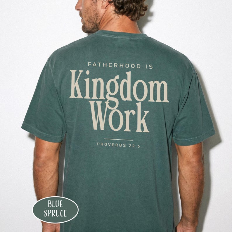 May include: Blue spruce t-shirt with the text "FATHERHOOD IS Kingdom Work" and "PROVERBS 22:6" printed on the back. The shirt is a solid color and has a crew neck.