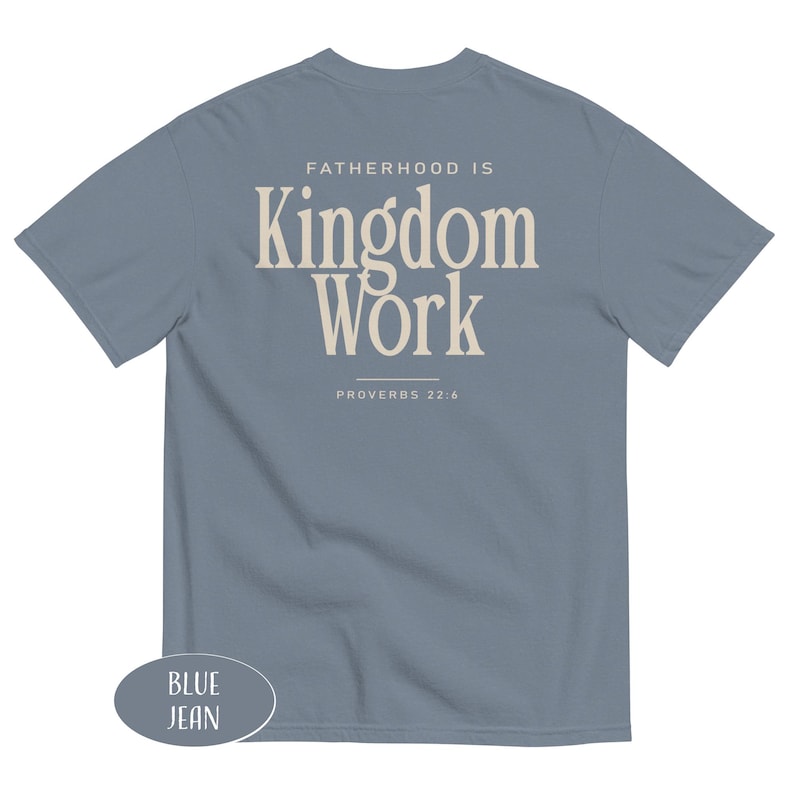 May include: Blue jean short-sleeve t-shirt with the text "FATHERHOOD IS Kingdom Work" in a cream-colored font. The text "PROVERBS 22:6" is below the main text. The shirt is a solid blue color.