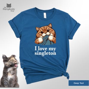 May include: Deep teal t-shirt featuring a cartoon cat biting a blue object. The text "I love my singleton" is printed in white. The Purrplexity Shop logo is in the upper left corner.
