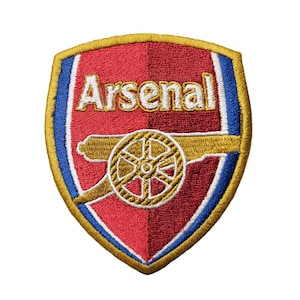Op de afbeelding: Geborduurde patch met het embleem van Arsenal Football Club. Het schildvormige embleem heeft een rode achtergrond, gouden details en het woord "Arsenal" in het wit. Een gouden kanon is gecentreerd onder de tekst, met blauwe en gouden randen.