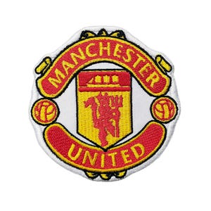 Może przedstawiać: Haftowana naszywka z logo Manchester United. Naszywka ma białe tło z czerwono-żółtym herbem. Napisy "MANCHESTER" i "UNITED" są czerwone na żółtym banerze.
