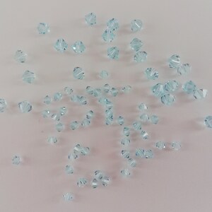 May include: A scattering of light blue crystal beads on a white background. The beads are faceted and have a star-shaped design.