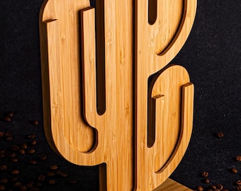 May include: A wooden cactus-shaped coffee pod holder with a base. The holder is made of light brown bamboo and has a natural wood finish. The holder is sitting on a surface covered in coffee beans.