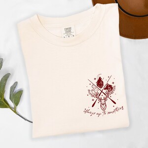May include: A cream-coloured t-shirt with a maroon graphic featuring a deer, wolf, and other elements. The text "Always up to something" is below the graphic. The shirt is a Comfort Colors brand, size L-G-G.