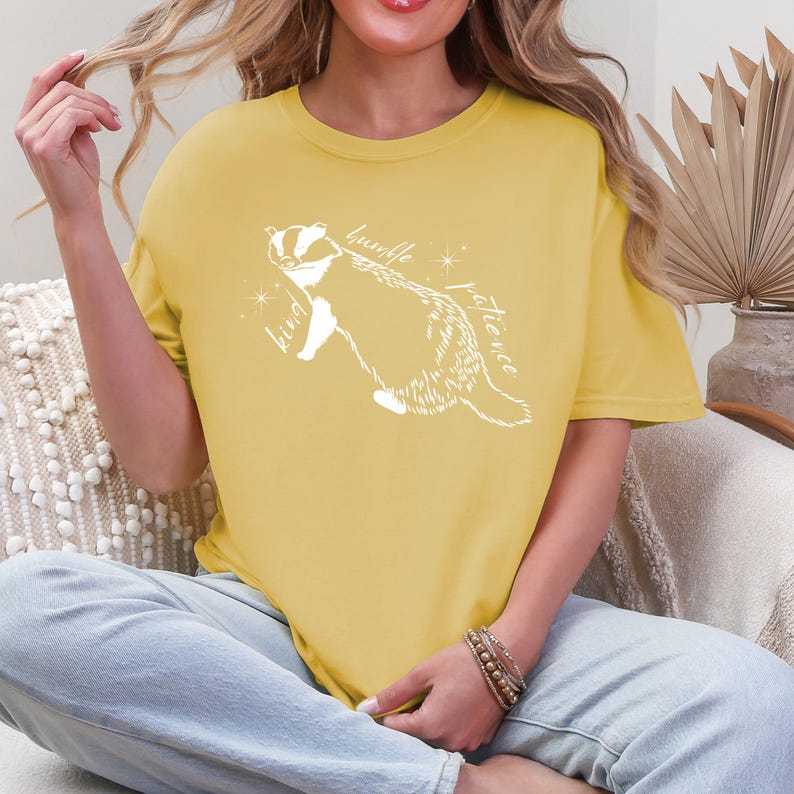 May include: A yellow t-shirt with a white badger illustration and the words "humble", "kind", and "patience" written around it.