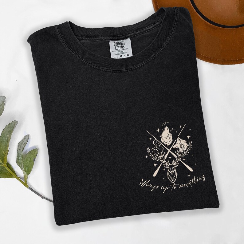 May include: Black t-shirt with a graphic design featuring a wolf, deer, and horse with crossed arrows and the text "Always up to something." The shirt is from Comfort Colors.